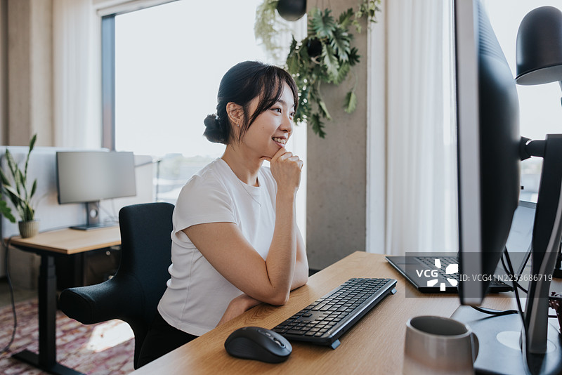 年轻女子在现代办公室对着电脑微笑图片素材