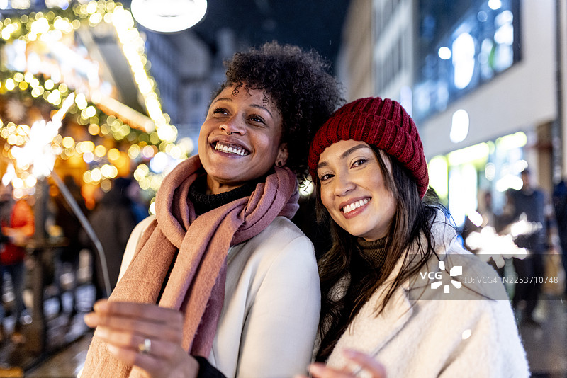 两位美丽的多民族快乐女性网红和挚友在慕尼黑玛利亚广场的圣诞市场中漫步图片素材