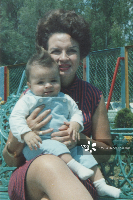 1960年代拍摄：一位笑容满面的中年女性坐在自家后院，抱着孙女看向镜头。图片素材