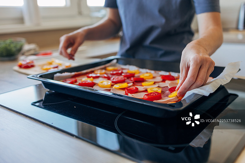 一个人正在烘焙烤盘上制作披萨，并放上配料图片素材