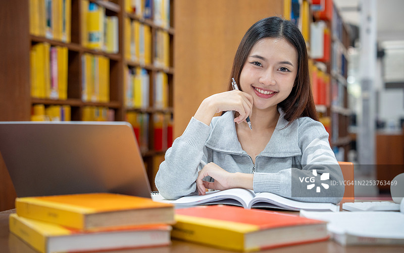 教育与学校概念。年轻女子在图书馆读书。漂亮的亚洲女大学生抱着书，在图书馆里开心地笑着。学习与教育图片素材