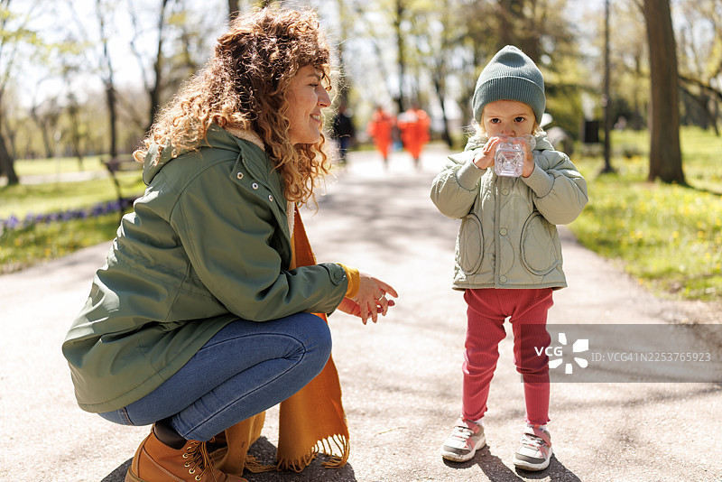 阳光明媚的公园里，一个口渴的可爱小女孩在喝水图片素材