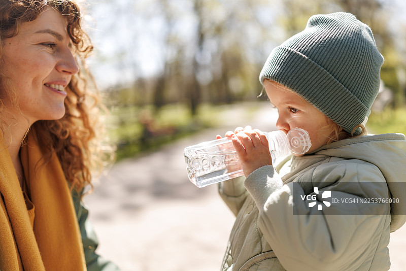 口渴的可爱小女孩在阳光明媚的公园里喝水图片素材