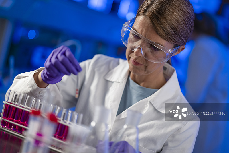 一位女科学家戴着护目镜和手套，在现代实验室里使用移液管进行实验。图片素材