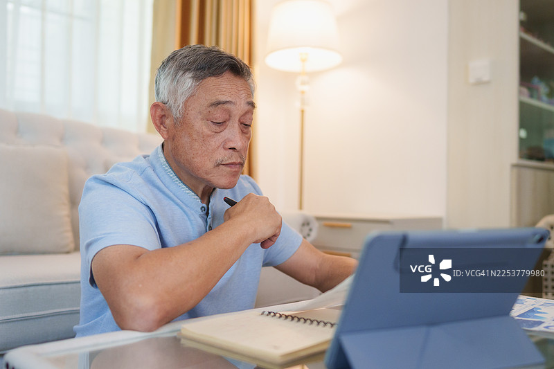 一位年长的亚洲男性在他的客厅里管理他的月度预算图片素材