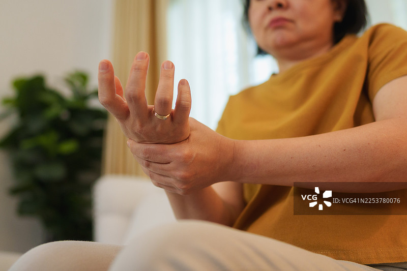 一位亚洲老年女性在客厅沙发上按摩手部，手腕和手掌疼痛图片素材