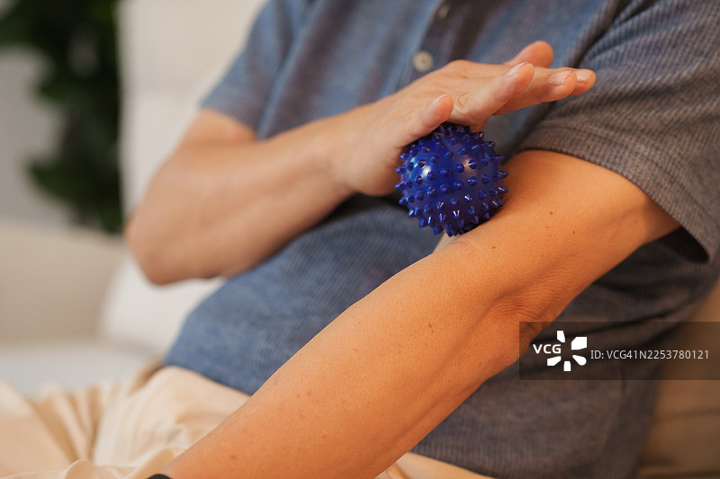 一位老年男子在客厅沙发上用治疗球按摩肌肉图片素材