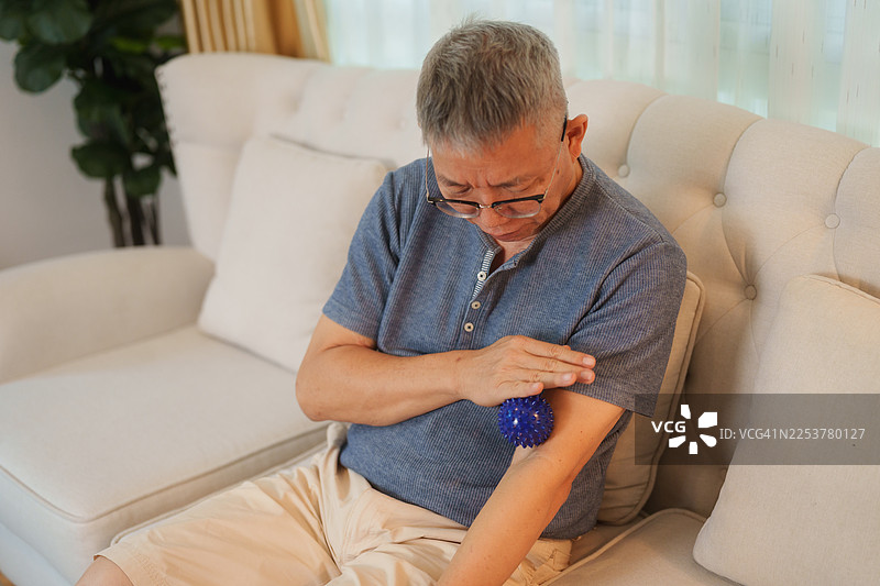 一位年长男子在客厅沙发上用治疗球按摩肌肉图片素材