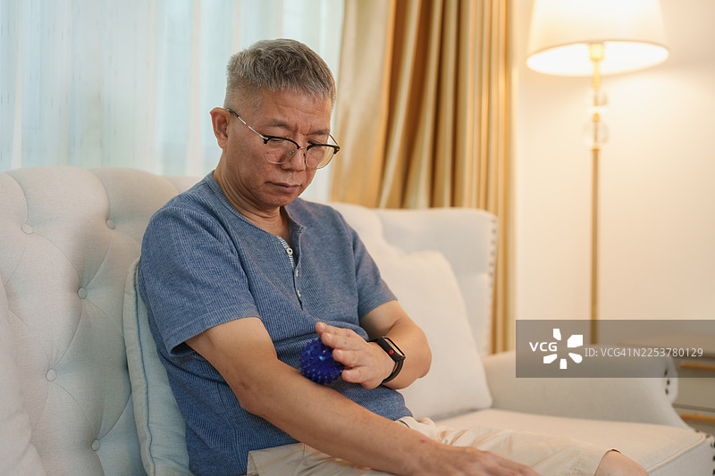 一位老年男子在客厅沙发上用治疗球揉捏肌肉图片素材