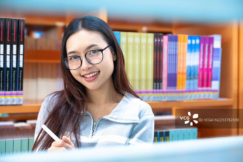 亚洲女学生在图书馆通过数字平板电脑与老师进行视频会议进行在线学习。返校季教育知识大学。年轻女性使用笔记本电脑工作。学习与教育的概念。图片素材