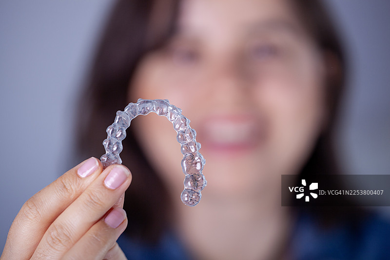 一位女士拿着隐形矫正器，这是用于牙齿矫正和牙科护理的现代解决方案图片素材