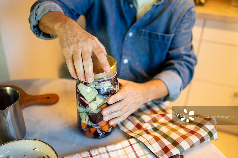 食品保存和家庭腌制的最后一步——特写镜头，展示一双用金属盖封住自制发酵蔬菜玻璃罐的手。图片素材