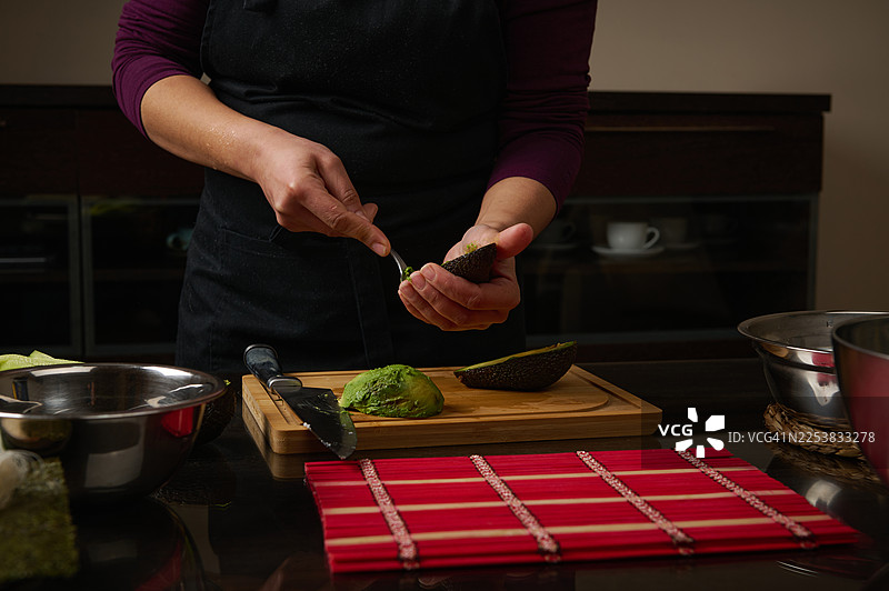 在现代厨房的砧板上用刀准备牛油果的双手图片素材