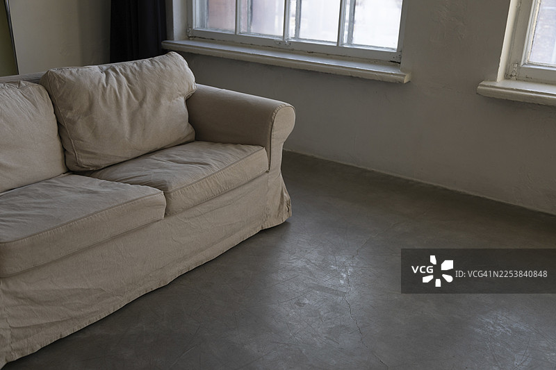 浅色沙发摆放在宽敞房间的灰色混凝土地板上，房间有两扇多格窗户。图片素材