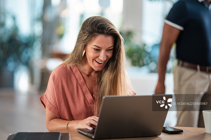 一位高加索女性在现代办公室使用笔记本电脑庆祝成功图片素材