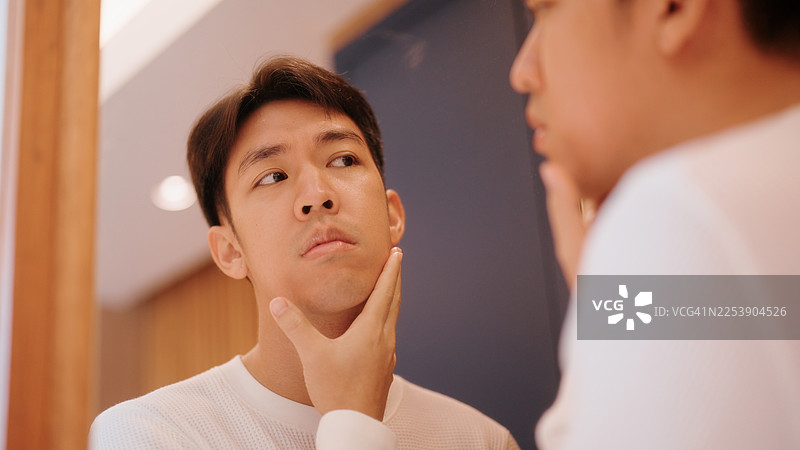 亚洲男子专注地看着镜中的自己，注意到脸上的细纹和衰老迹象图片素材
