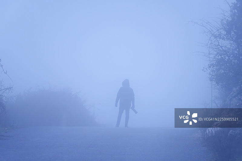 雾气弥漫的道路上，一位男摄影师的剪影图片素材