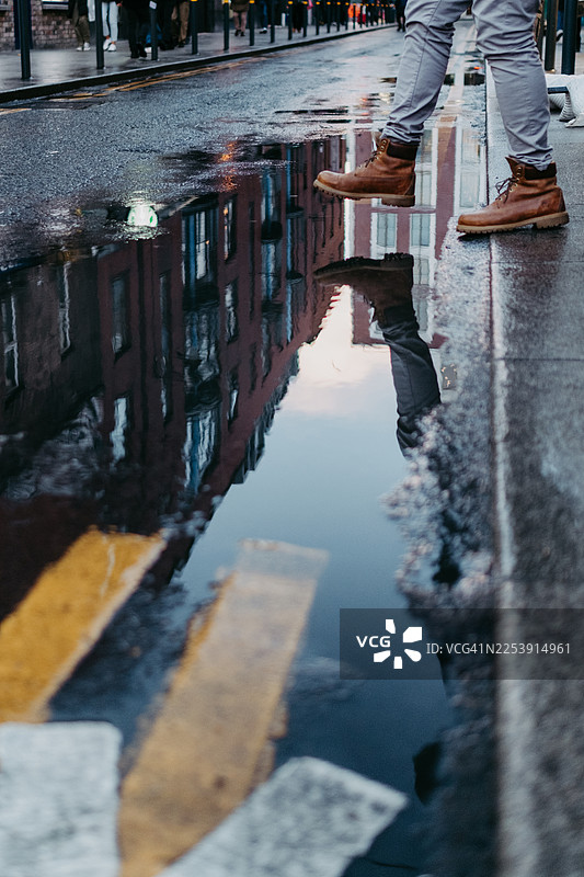 湿漉漉的城市街道上，水坑映出了脚的倒影图片素材