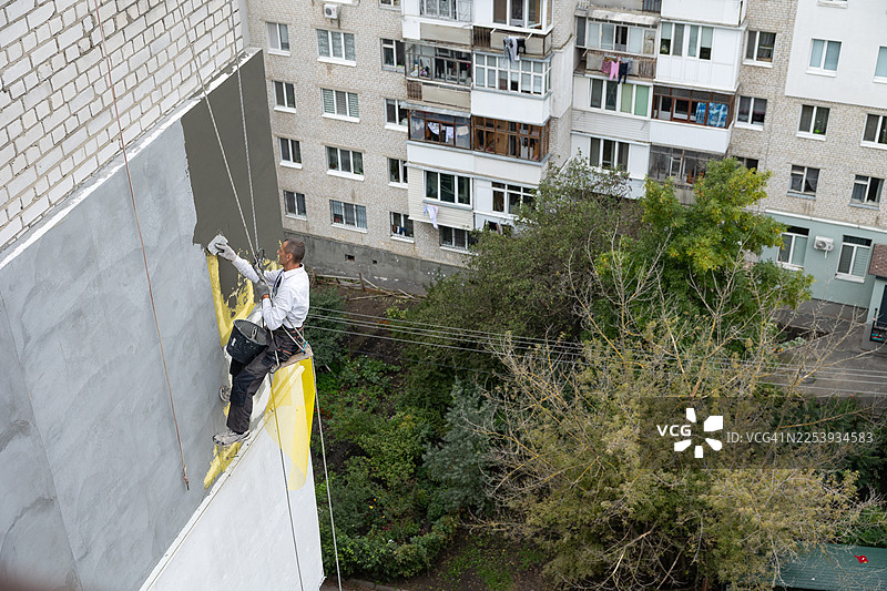建筑工人正在为建筑外墙的保温层施工，在黄色网格上涂抹砂浆。图片素材