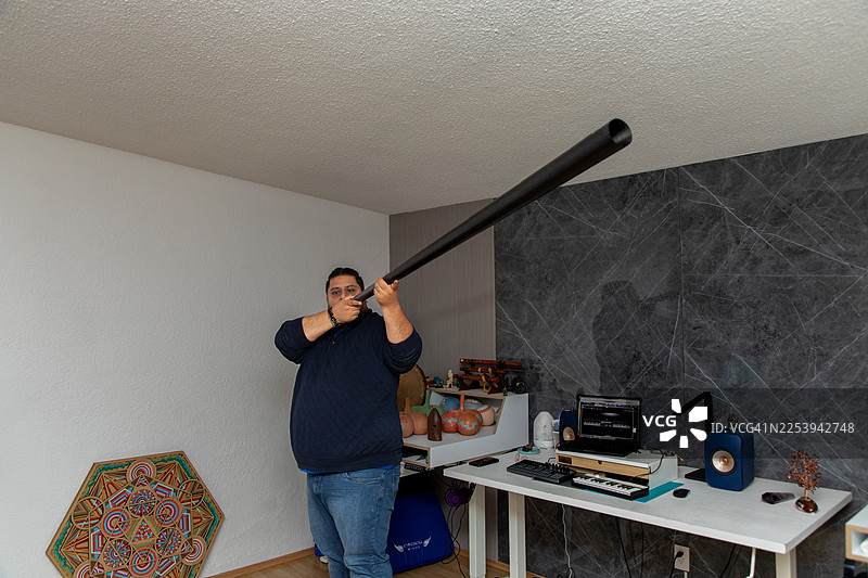 男人在家用工作室演奏迪吉里杜管，享受音乐和声音，营造室内放松的氛围图片素材