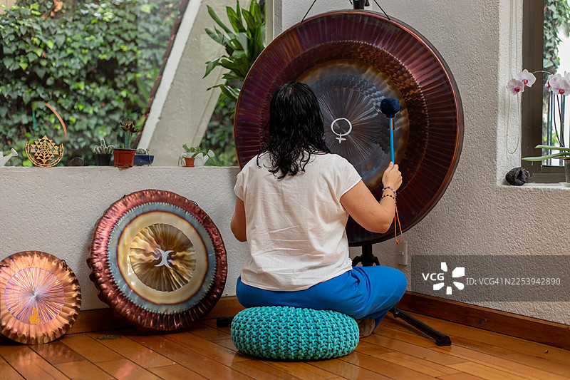 女性在家敲打大型锣，进行声音浴疗法，营造放松和精神健康氛围图片素材