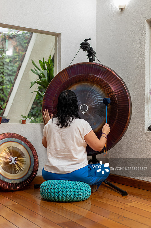 一位女性在宁静的精神健康疗程中，敲打巨型锣，进行声音疗法。图片素材