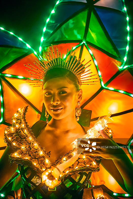 一位节日参与者的肖像，他身着一件巨大的、发光的服装，服装上装饰着多彩、抽象和自然的图案，背景是黑暗的夜晚。图片素材