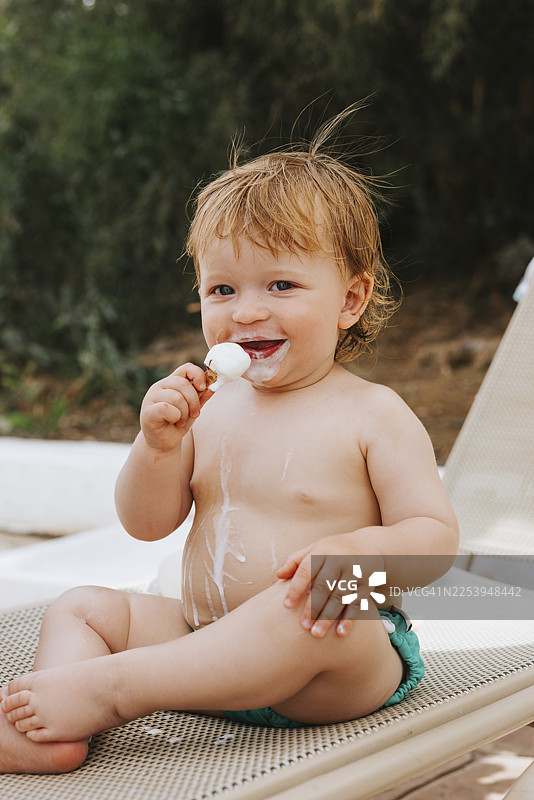 赤膊的可爱男孩坐在户外椅子上吃冰淇淋的肖像图片素材