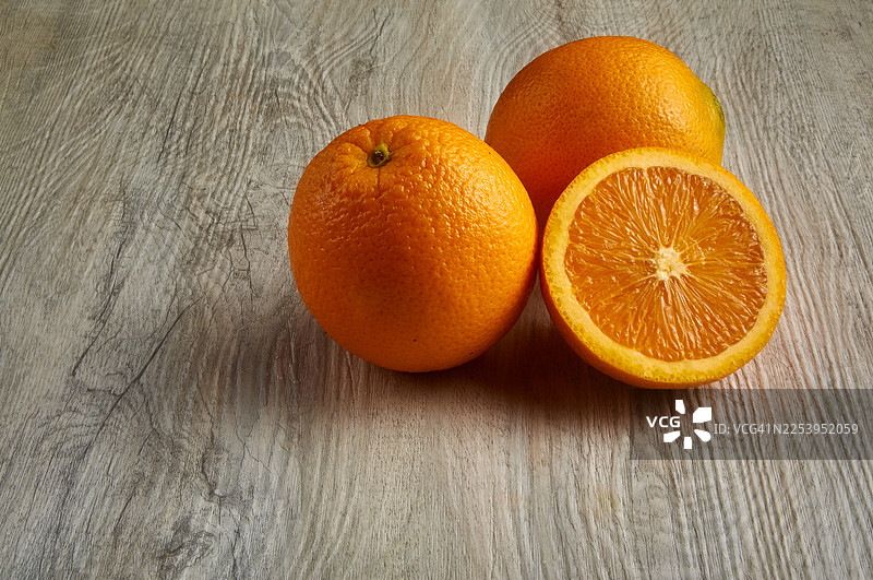 三颗新鲜的橙子摆放在质朴的木质表面上。图片素材