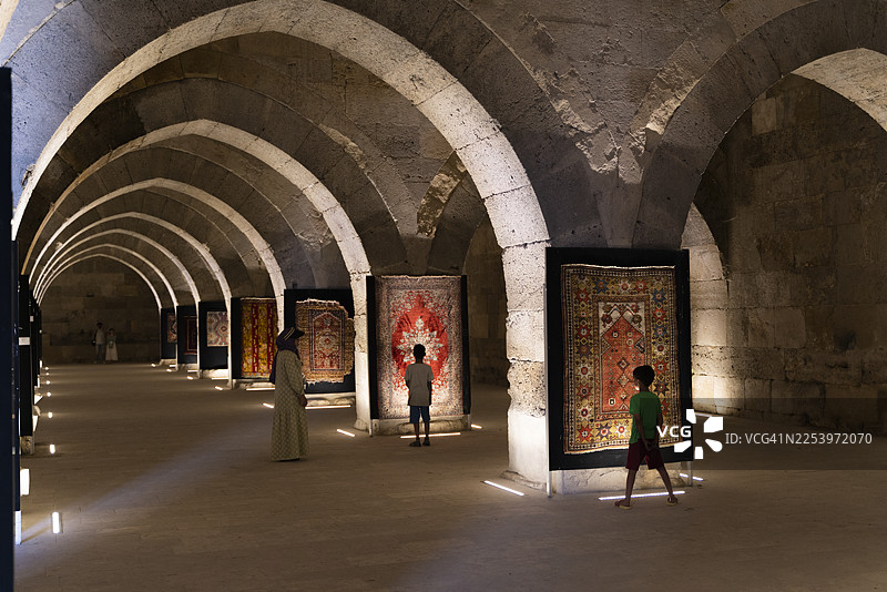 古老商队的驿站里，铺在地上的地毯已显陈旧，如今被挂在墙上作为展品。孩子们正在参观这次展览，亲身体验历史。图片素材