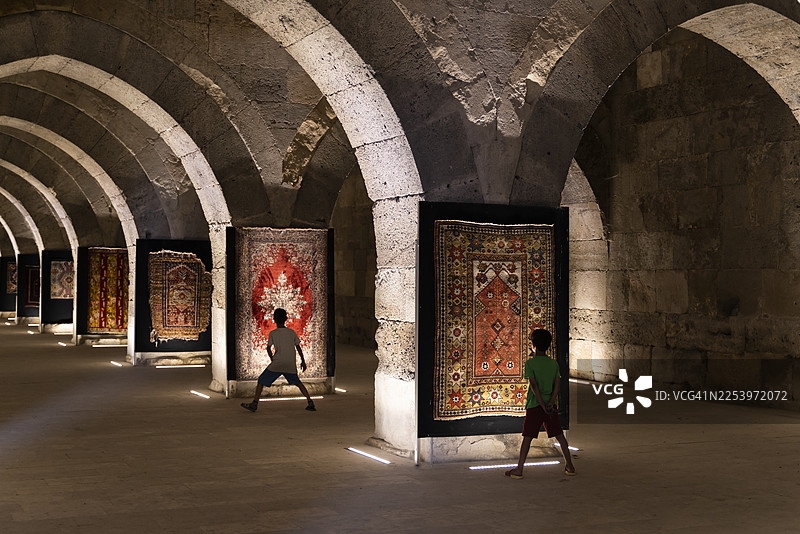 古老的客栈里，用于展示的旧地毯已显陈旧，被挂在墙上。孩子们正在参观展览，亲身体验历史。图片素材