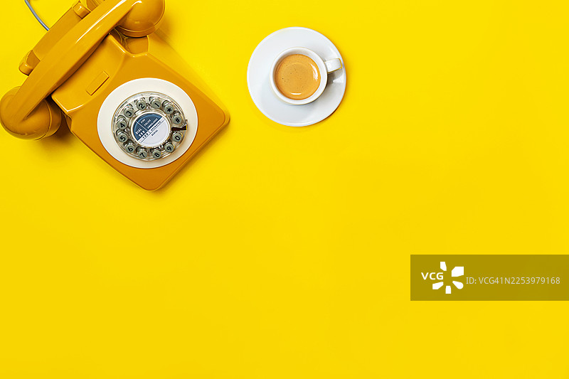 明亮背景上的黄色复古电话和咖啡杯。图片素材