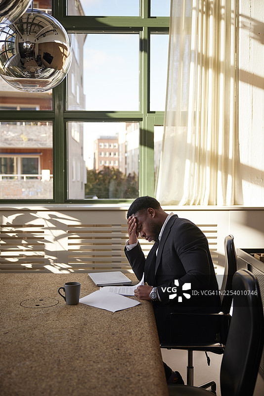 俯视角度，一名压力巨大的男律师坐在董事会会议室的桌子旁，正在阅读协议文件。图片素材