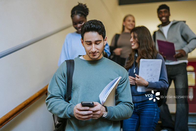 年轻的男大学生在楼梯上边走边玩手机图片素材
