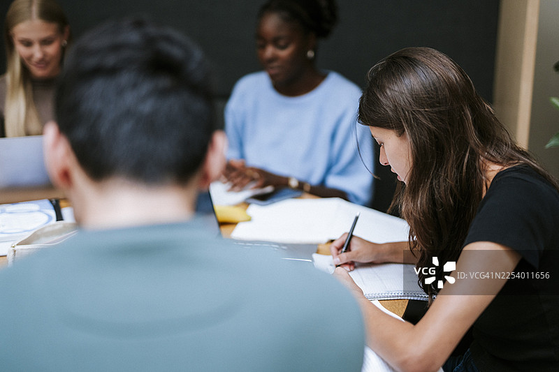 年轻女子在大学校园里与朋友们一起学习，同时在一本书上写作图片素材