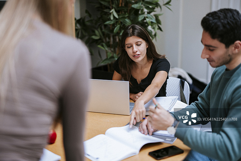 女学生在大学校园里和男学生一起学习，她指着书本。图片素材