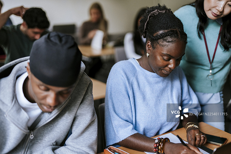 女老师站在一位正在大学学习并书写的成年学生旁边图片素材