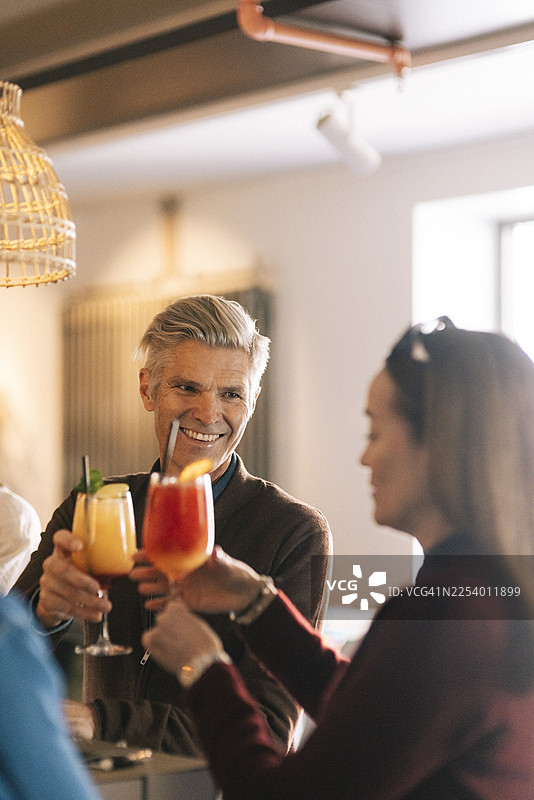 在酒吧派对上，微笑的男人和女性朋友一起举杯庆祝鸡尾酒图片素材