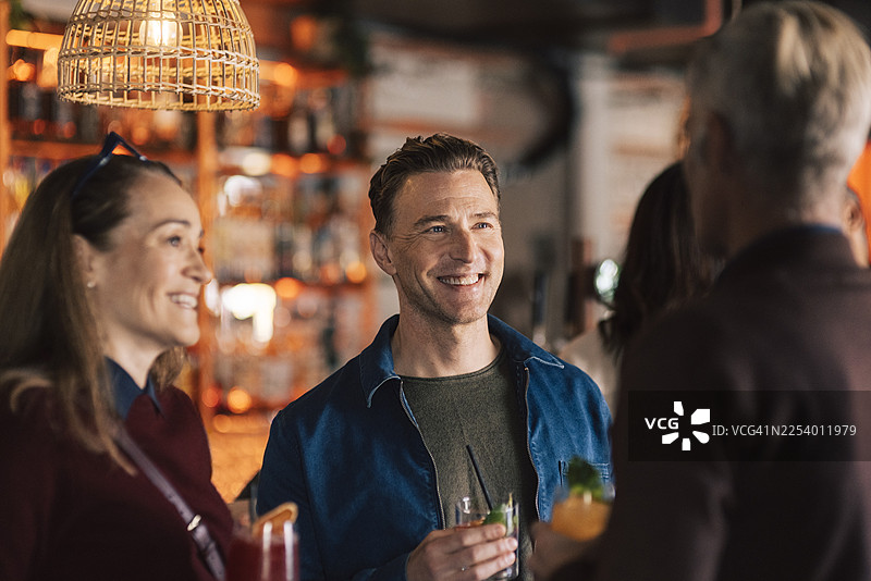 派对上，男人在酒吧里拿着酒杯，和朋友们谈笑风生图片素材
