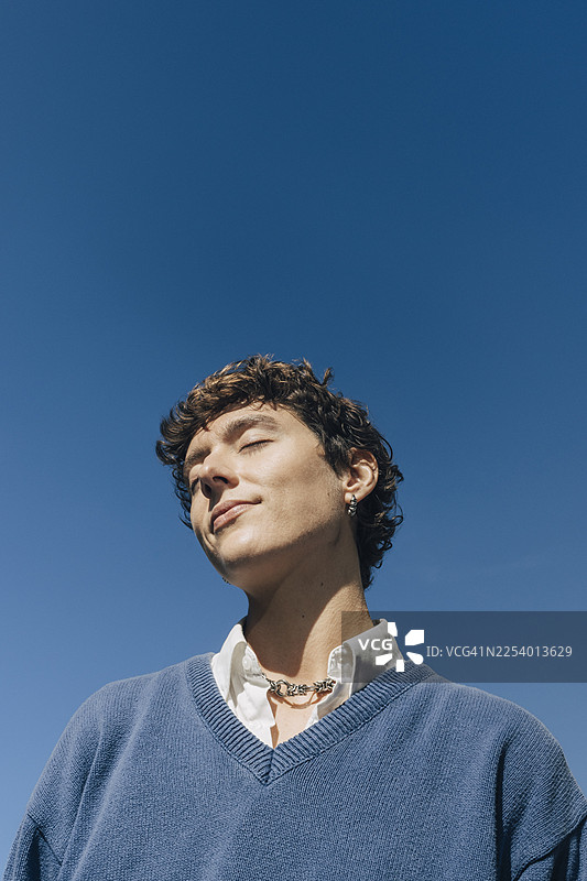仰视视角，一位无忧无虑的年轻女子闭着眼睛，背景是蓝天图片素材