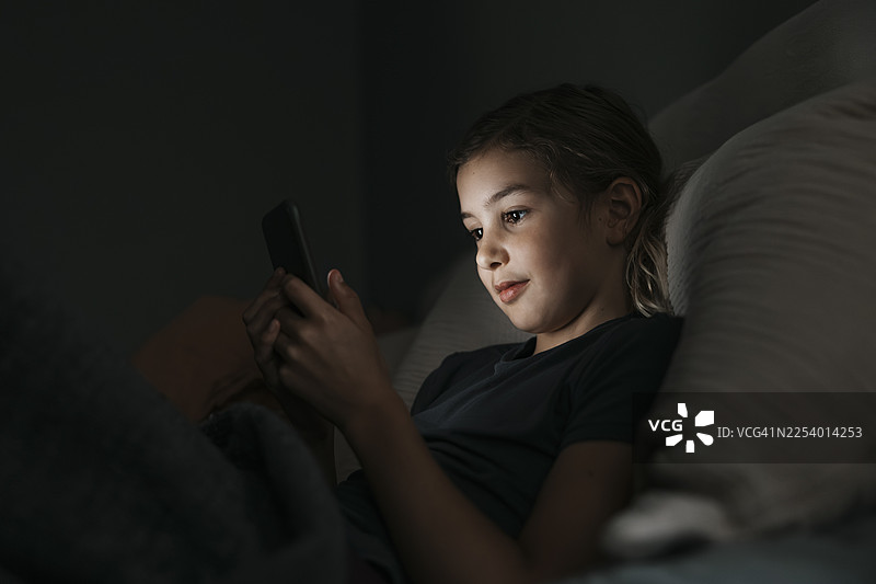 夜晚，女孩在卧室里使用智能手机图片素材