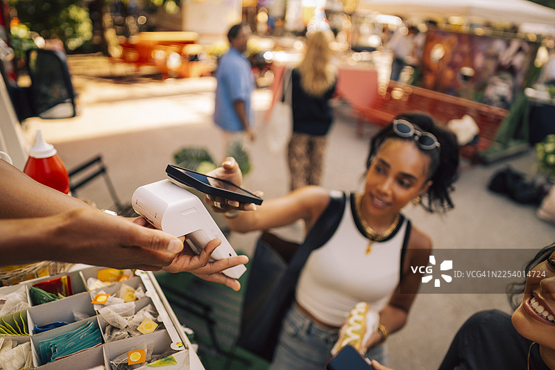 销售人员的手拿着信用卡读卡器，女顾客在读卡器上刷手机，场景为餐车图片素材