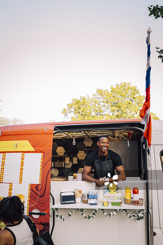 晴朗天空下，一位快乐的男性老板站在餐车旁，目光望向远方图片素材