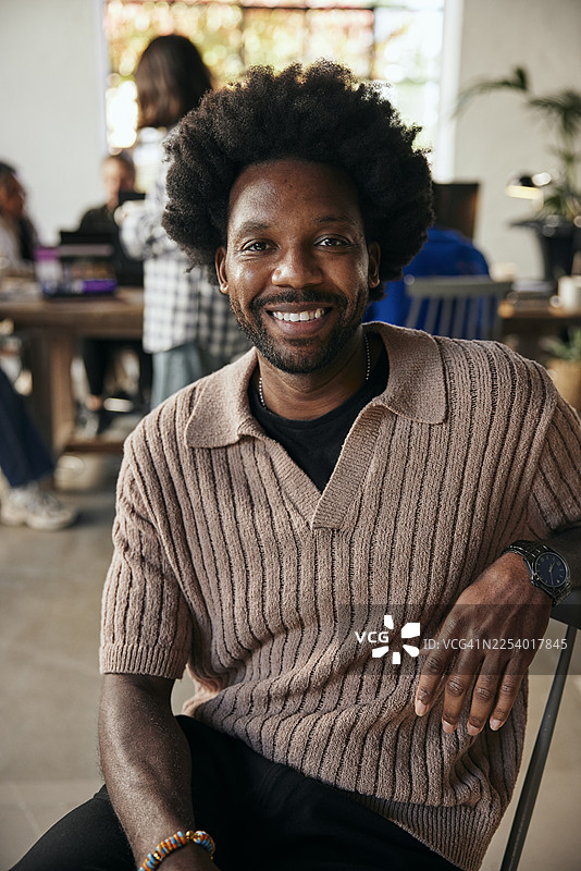 一位卷发、面带微笑的男性科技创业者，坐在创业公司办公室的椅子上。图片素材