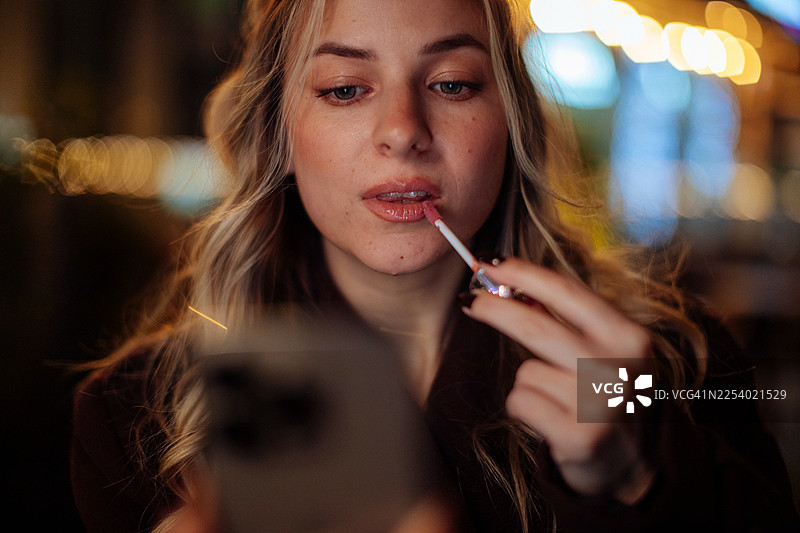 一位年轻女子一边照着手机镜子一边涂抹唇彩图片素材