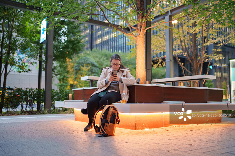 女商人城市户外晚间休息时使用智能手机图片素材