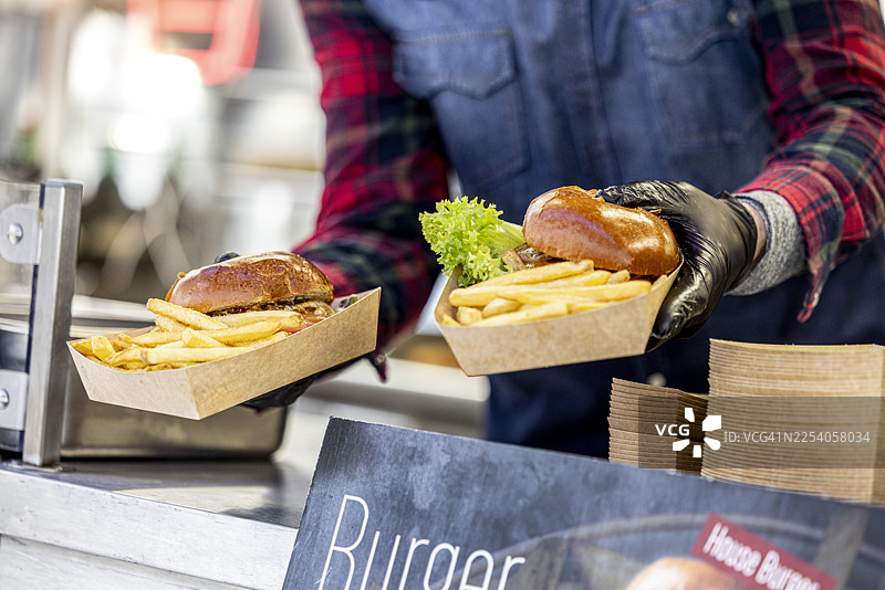 街头餐车大厨制作的美味牛肉汉堡配薯条，用纸盒打包外带。图片素材