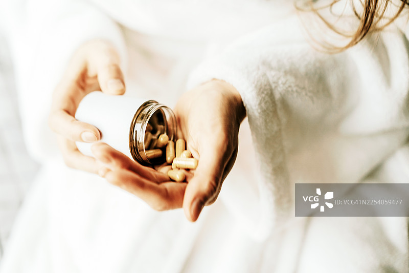 身穿白大褂的人手持药瓶，瓶中装有胶囊，寓意健康与养生图片素材