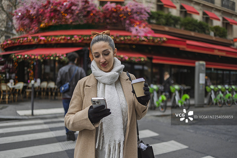 戴着贝雷帽的女士在巴黎用智能手机，手持咖啡杯图片素材
