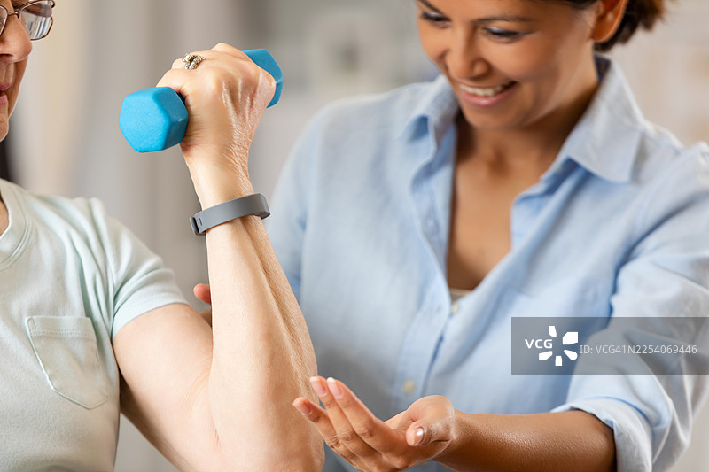 理疗师协助患者进行哑铃练习，以增强手臂力量和进行康复。图片素材